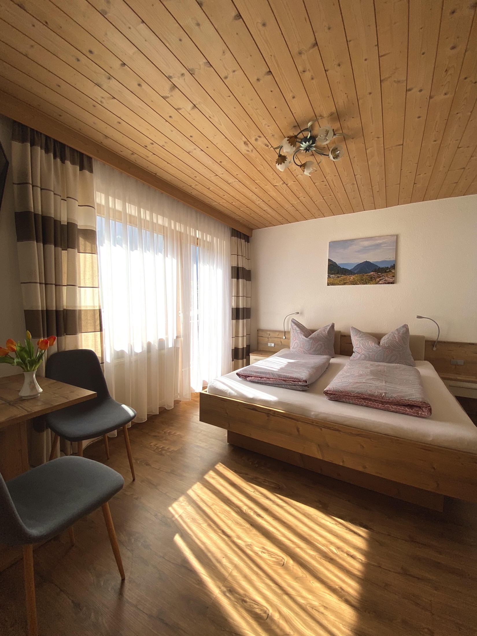 Sonniges Doppelzimmer mit Holzbett und Bergmotiv